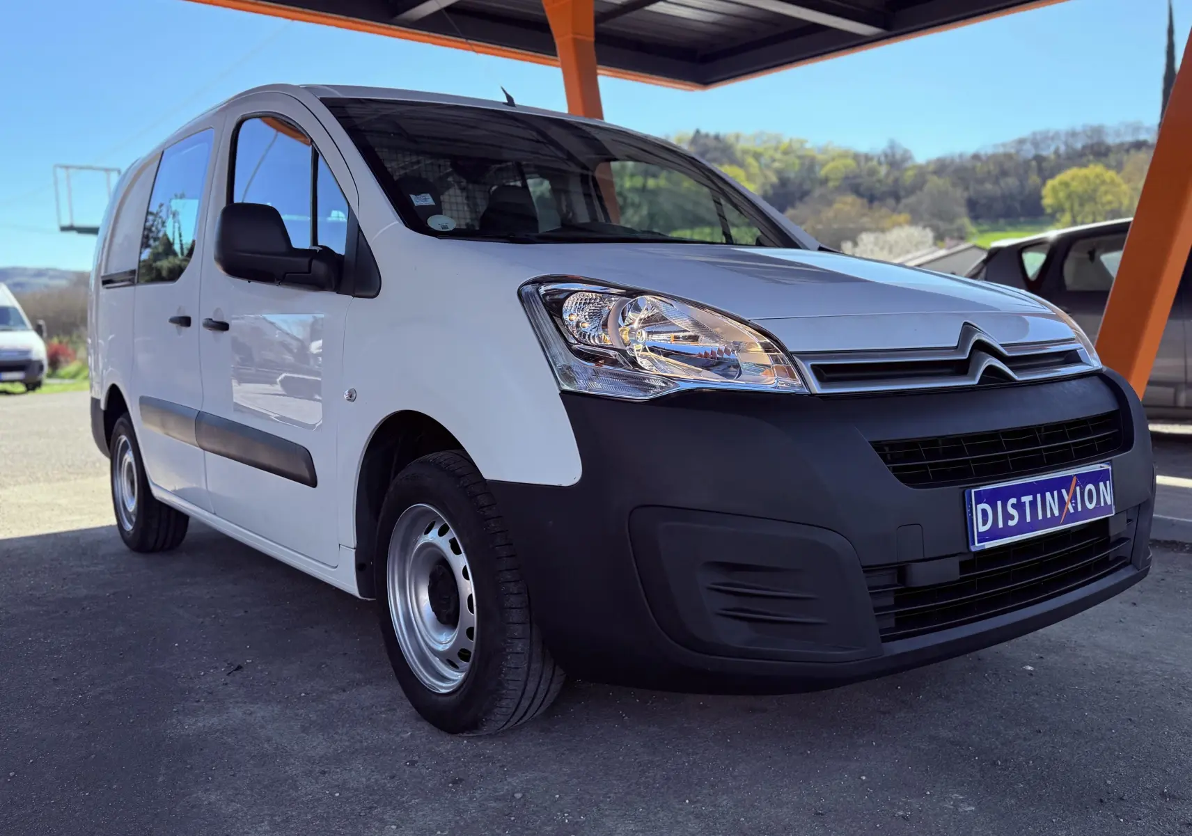 Vue 3/4 avant gauche d’un Citroën Berlingo blanc avec pare-chocs noirs sous un abri en extérieur.