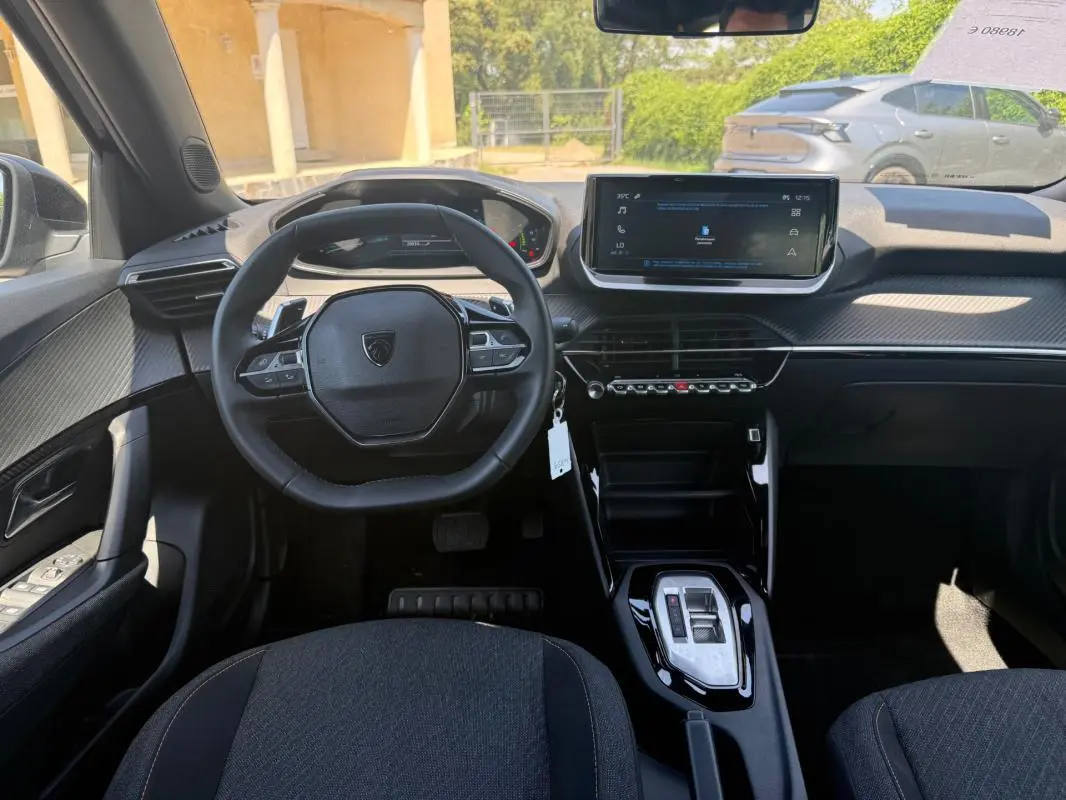 Vue intérieure frontale du poste de conduite du Peugeot 2008 Hybrid noir avec écran tactile et volant compact multifonction.