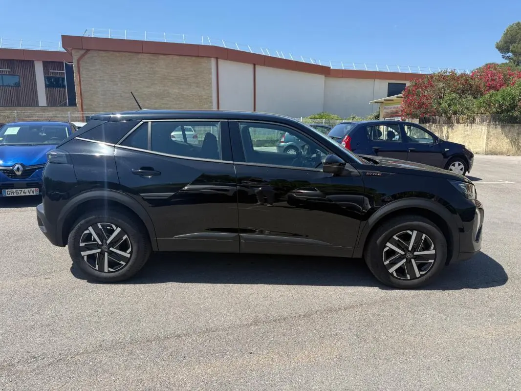 Profil côté gauche d’un Peugeot 2008 Hybrid 136 e-DCS6 Style noir avec jantes 16 pouces, en extérieur sur parking.