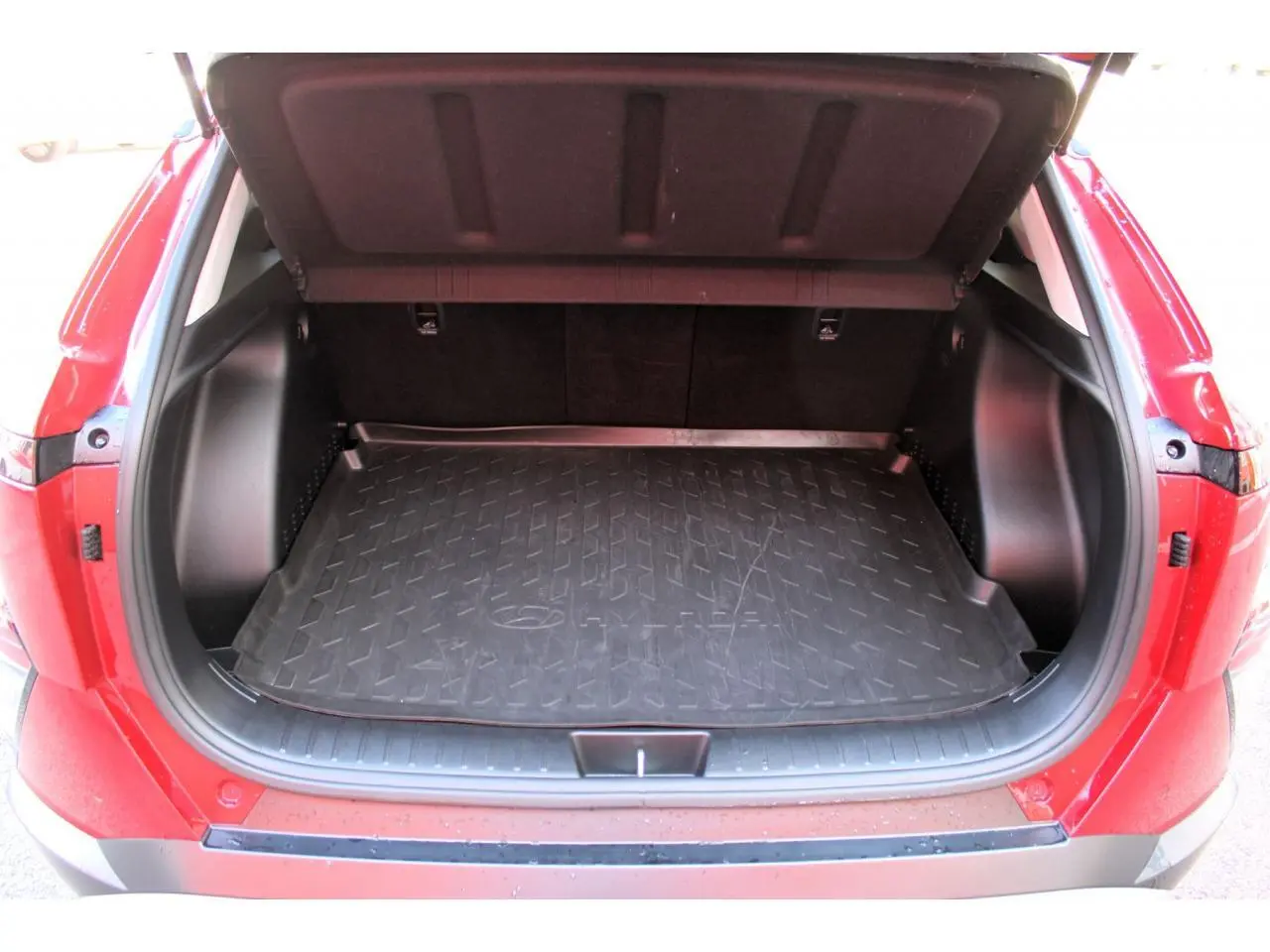Coffre ouvert vu de l'arrière d'un Hyundai Kona rouge Ultimate Metal avec tapis de coffre noir et intérieur sombre.