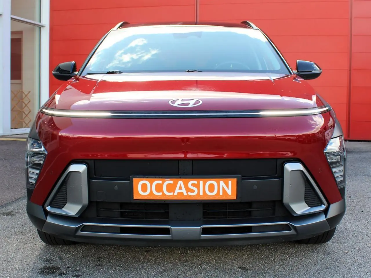 Vue frontale d'un Hyundai Kona 2024 rouge Ultimate Metal avec toit noir et calandre moderne, plaque "OCCASION" orange visible.