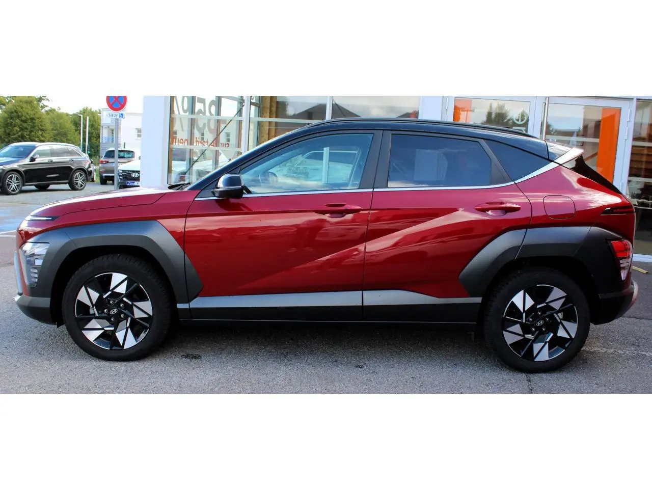 Vue latérale droite du Hyundai Kona 2024 rouge Ultimate Metal avec toit noir et protections d'ailes gris anthracite.