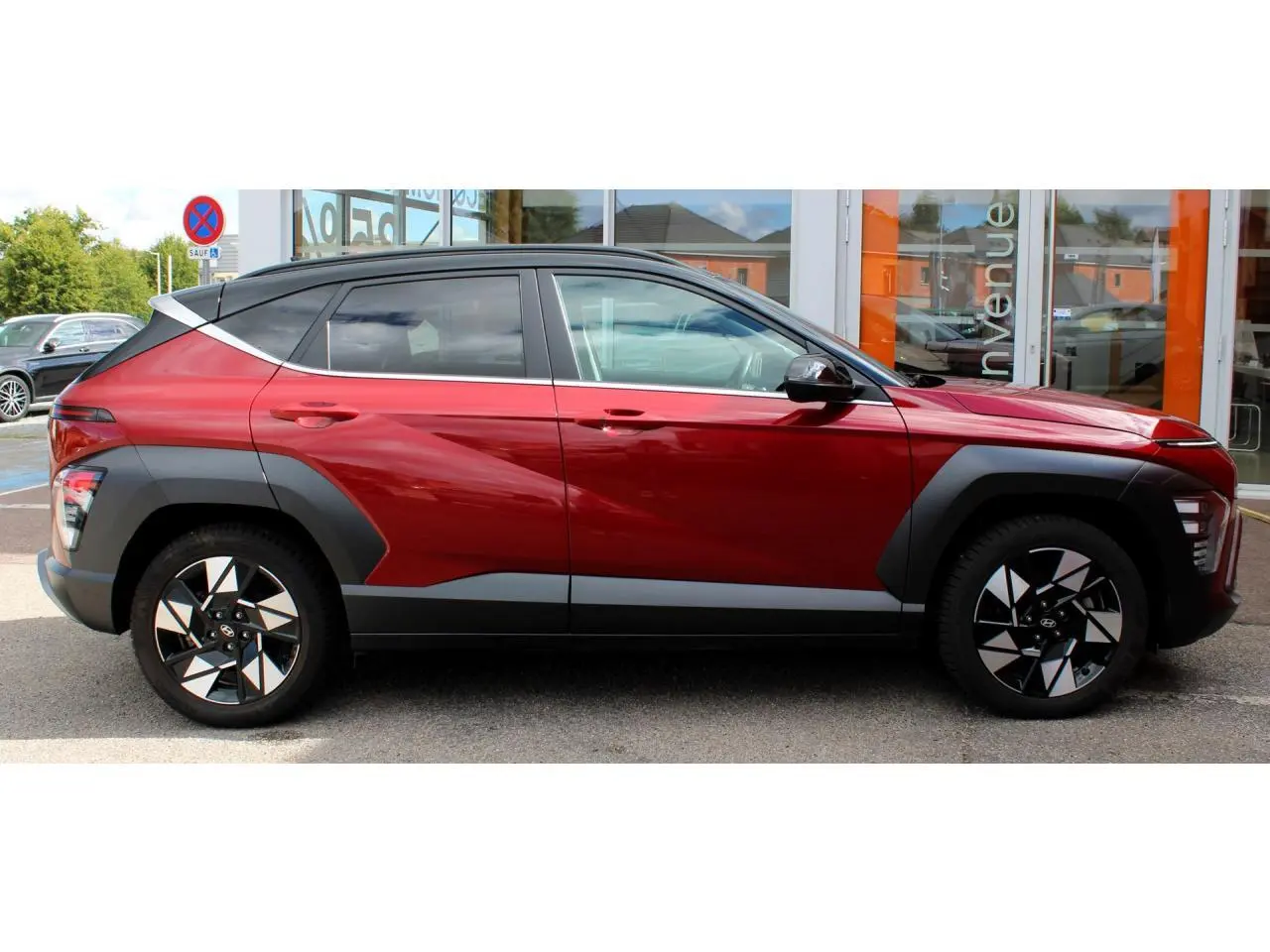 Vue latérale droite d'un Hyundai Kona 2024 rouge Ultimate Metal avec toit noir et protections d'ailes gris anthracite.