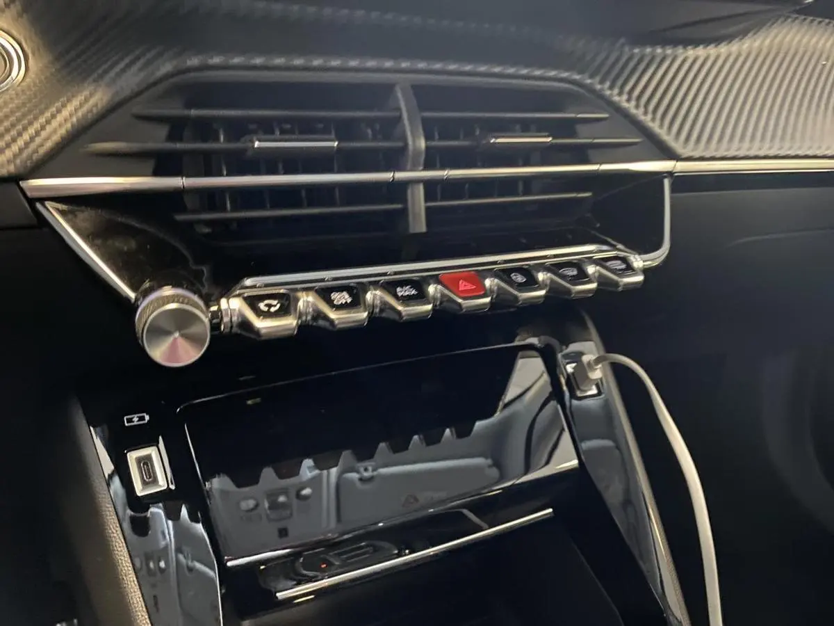 Vue rapprochée de la console centrale du Peugeot 2008 e-136 Allure Pack 2022 avec boutons chromés et câble USB connecté.