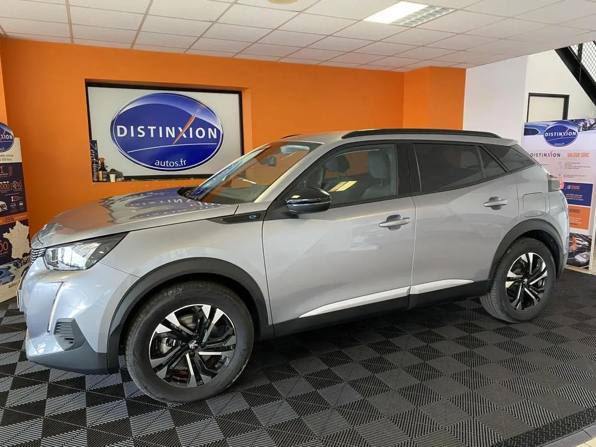 Peugeot 2008 e-136 Allure Pack gris Artense en profil droit, jantes alliage bi-ton et vitres surteintées en showroom.