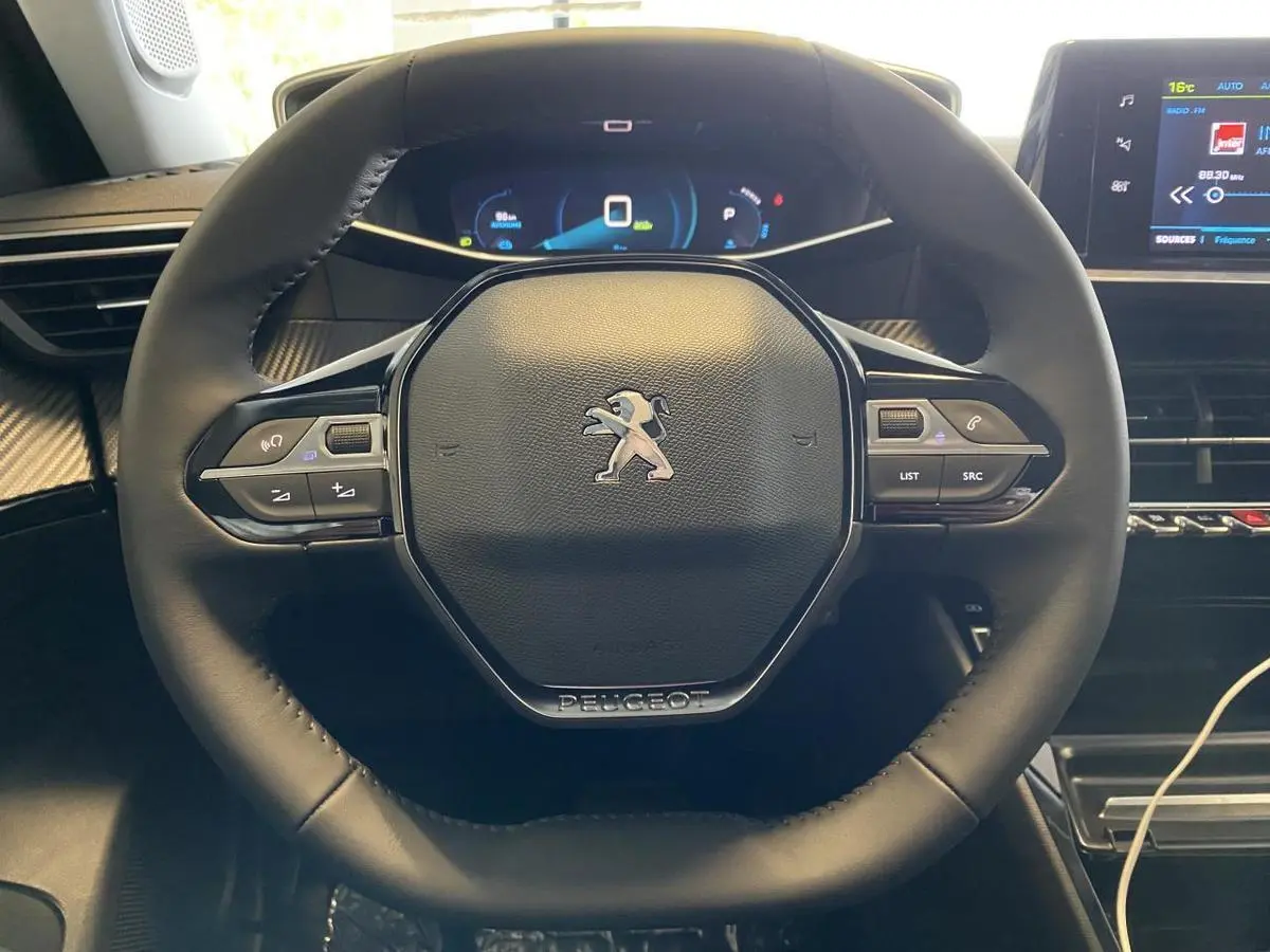Vue rapprochée du volant cuir noir du Peugeot 2008 e-136 Allure Pack 2022 avec commandes intégrées et tableau de bord numérique.