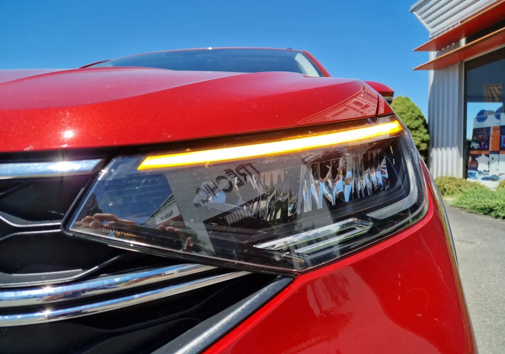 Gros plan sur le phare avant droit allumé du Volkswagen Taigo rouge roi 2023, soulignant son design moderne.