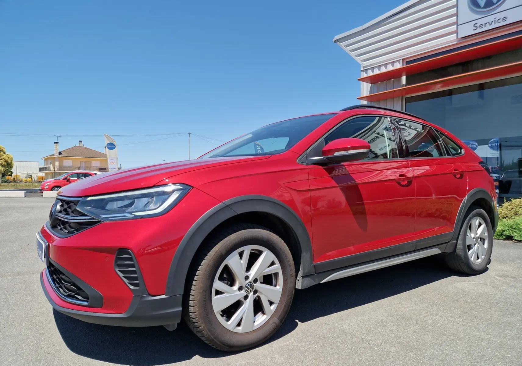 Volkswagen Taigo rouge roi en 3/4 avant droit, avec jantes alliage et protections noires autour des roues.