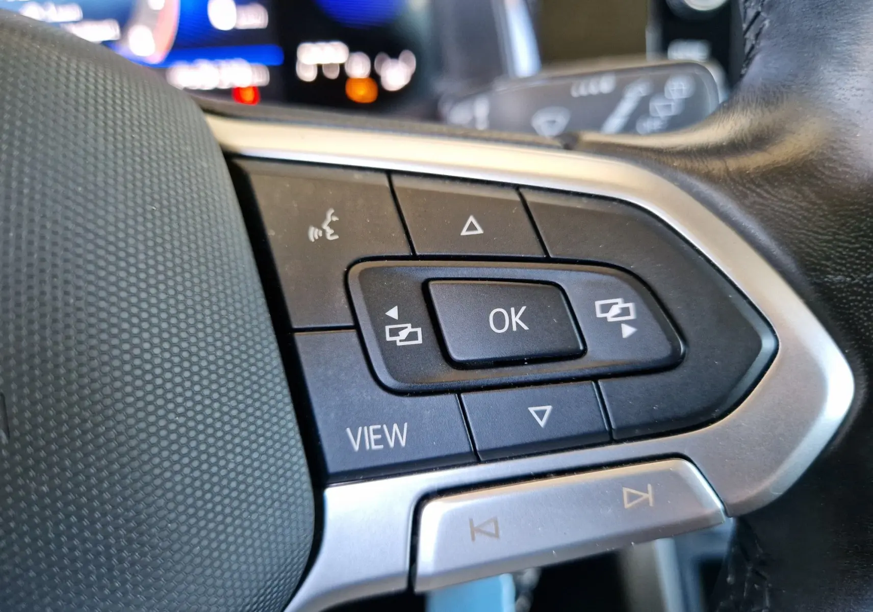 Gros plan sur les commandes multifonctions au volant du Volkswagen Taigo rouge roi, avec bouton OK et touches de navigation.