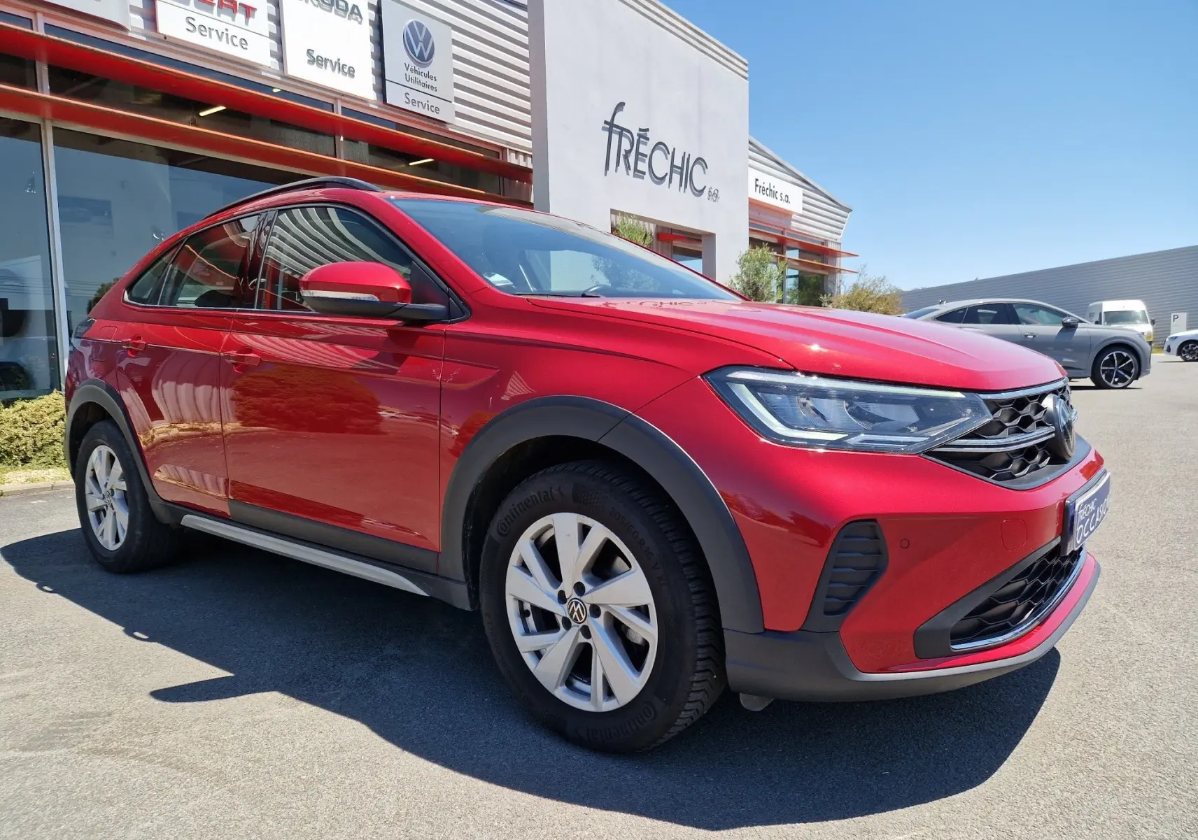 Volkswagen Taigo rouge roi en 3/4 avant droit, mettant en valeur ses phares LED et ses protections noires contrastées.