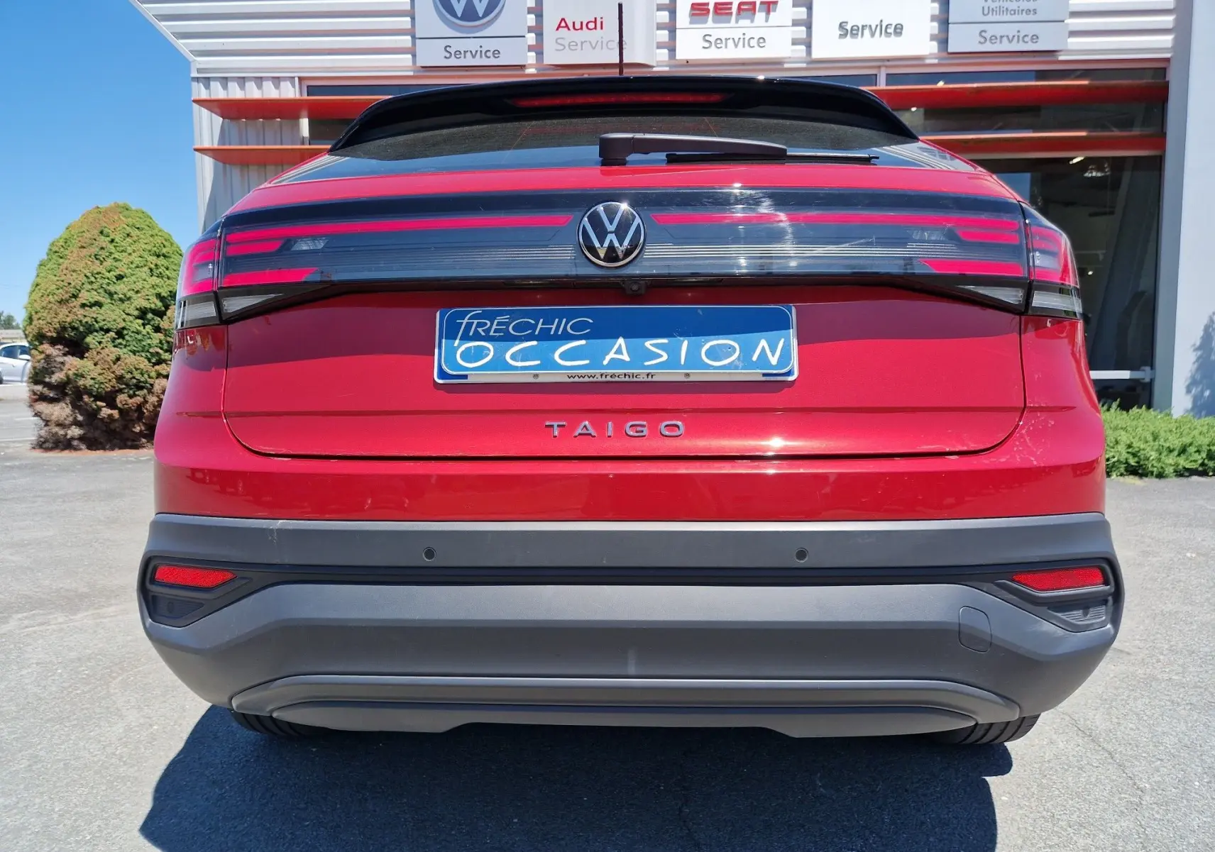 Vue arrière du Volkswagen Taigo rouge roi 2023 avec feux LED horizontaux et plaque d'occasion bleue.