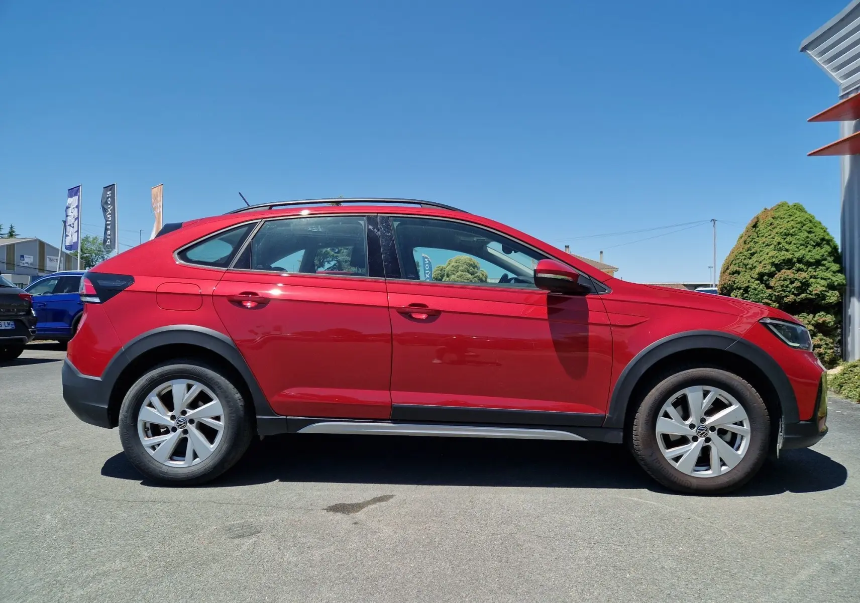 Profil droit d'un Volkswagen Taigo rouge roi 2023 avec jantes alliage et protections noires sur les passages de roues.