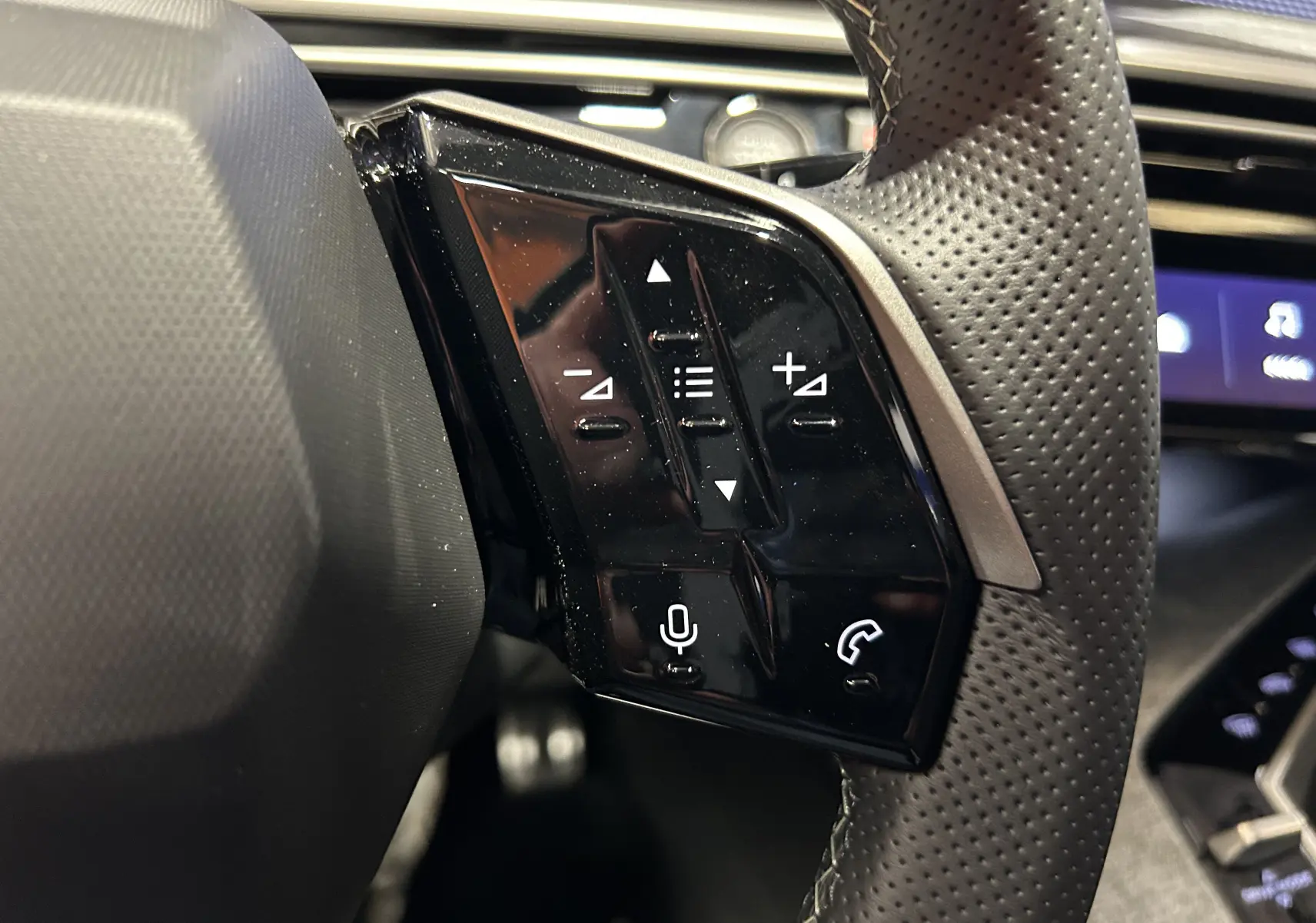Gros plan sur les commandes gauche du volant en cuir perforé du Peugeot 5008 Bleu Ingaro, avec boutons de volume et appel.