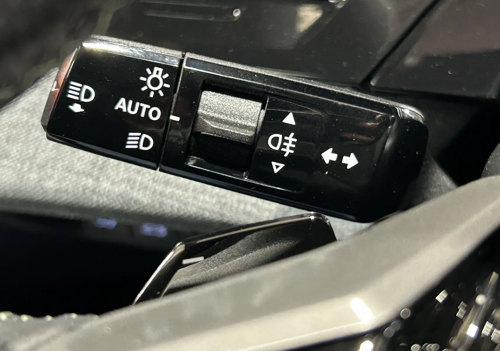 Gros plan sur la commande des feux automatiques et antibrouillard du Peugeot 5008 III Hybrid 145 GT, intérieur noir.