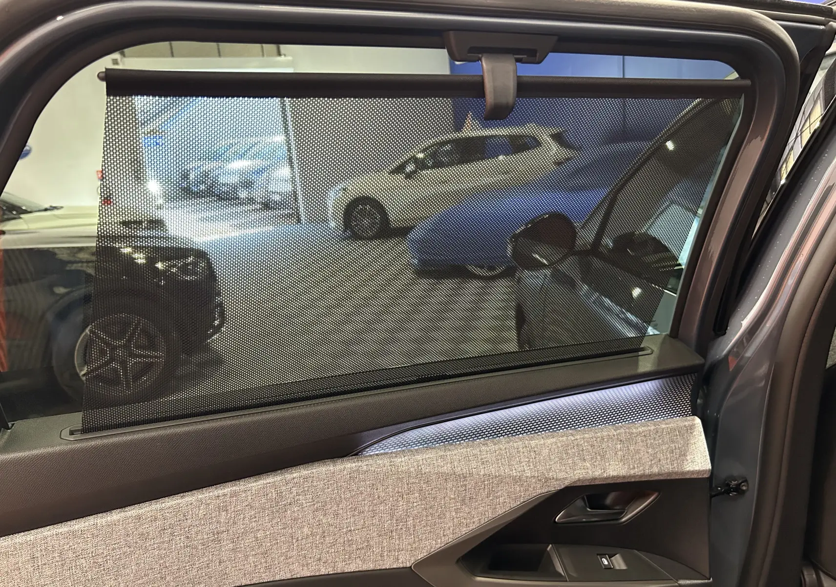 Vue intérieure côté gauche de la porte arrière du Peugeot 5008 Bleu Ingaro avec store pare-soleil déployé.