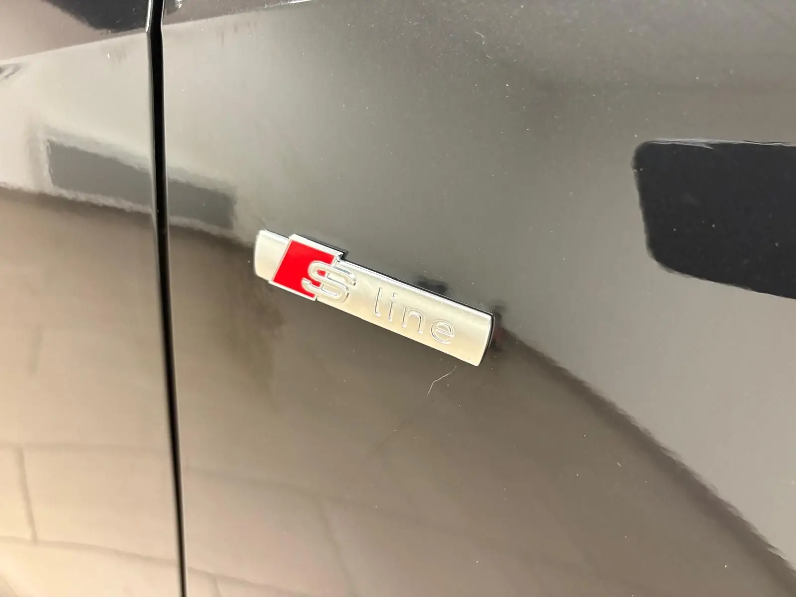 Gros plan sur l'emblème S line argent et rouge sur la carrosserie noire métallisée d'un Audi Q2.