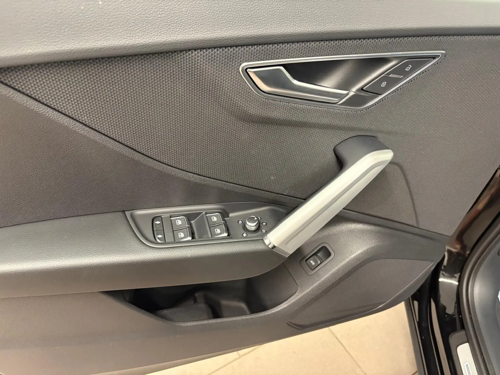 Gros plan sur la porte avant gauche de l’Audi Q2 Noir Mythic, montrant les commandes des vitres et la poignée intérieure argentée.