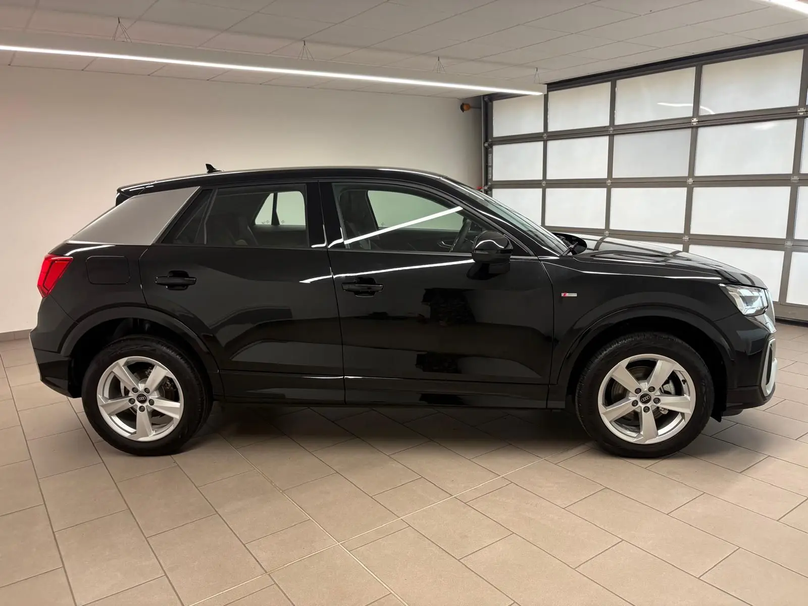 Audi Q2 35 TFSI S Line noir mythic vue de profil côté gauche dans un garage lumineux, jantes alliage visibles.
