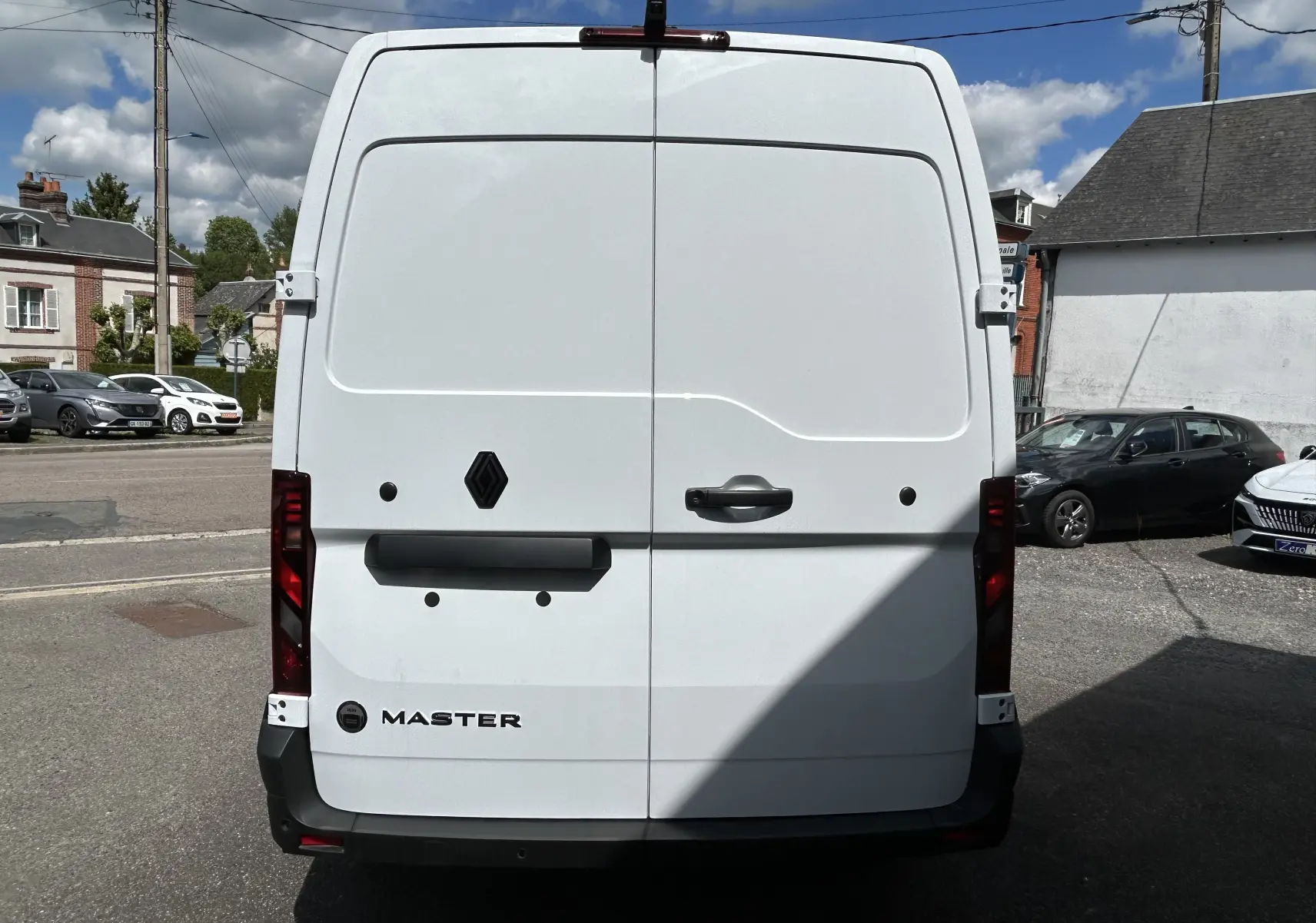 Vue arrière d’un utilitaire Renault Master blanc, avec portes battantes fermées et feux arrière verticaux rouges.