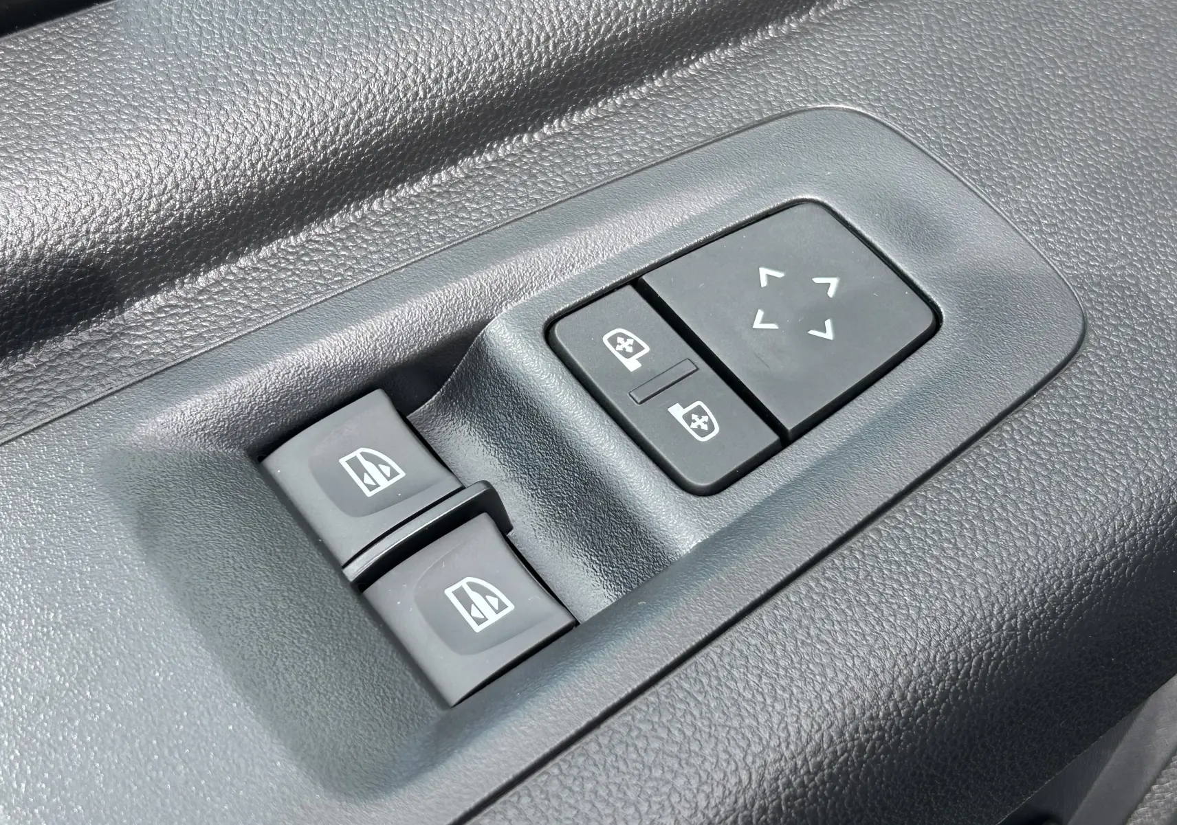 Gros plan sur les commandes électriques des vitres et des rétroviseurs sur la porte intérieure noire du Renault Master blanc.