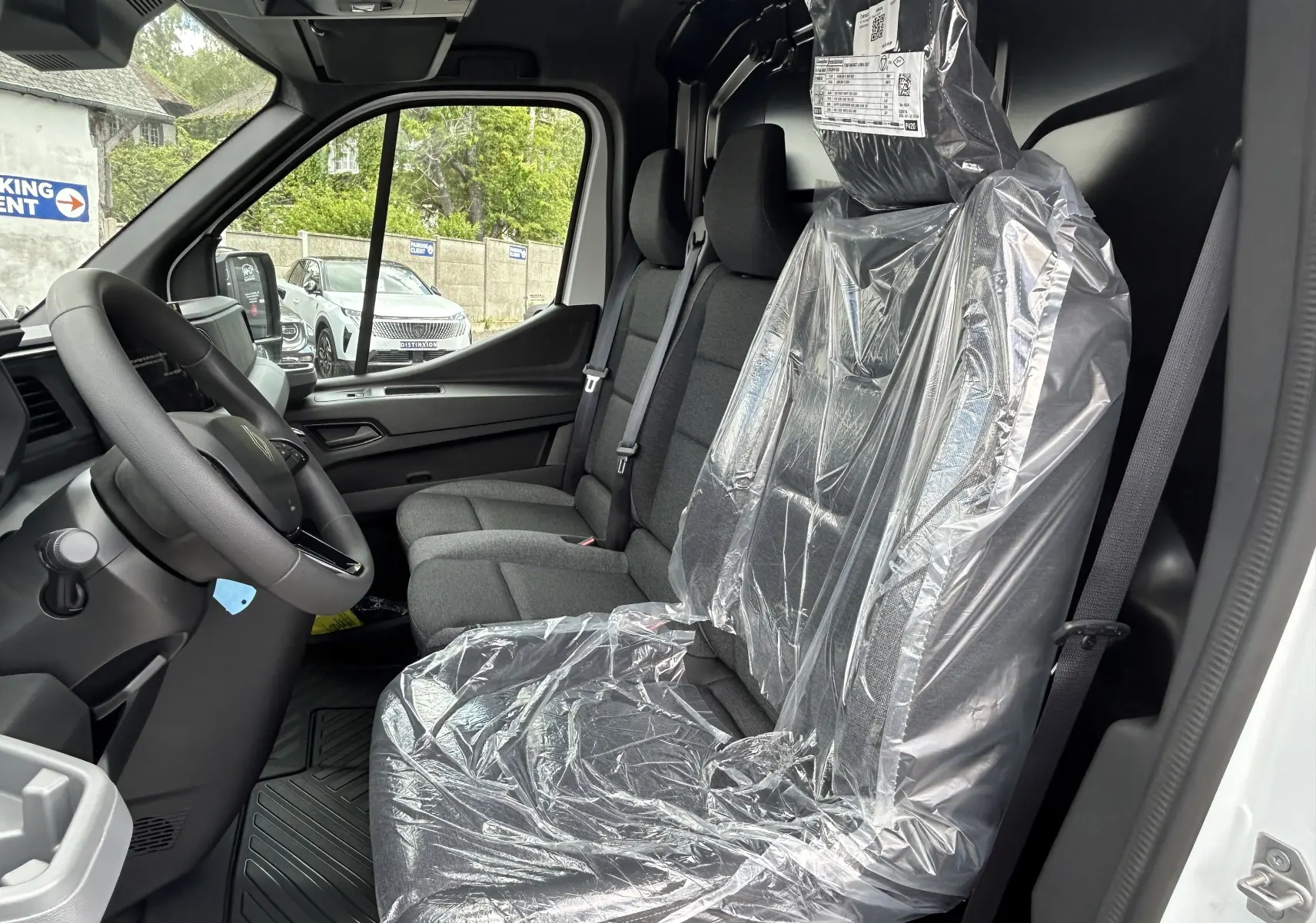 Vue intérieure côté conducteur du Renault Master blanc 2025, sièges avant en tissu protégés par film plastique.