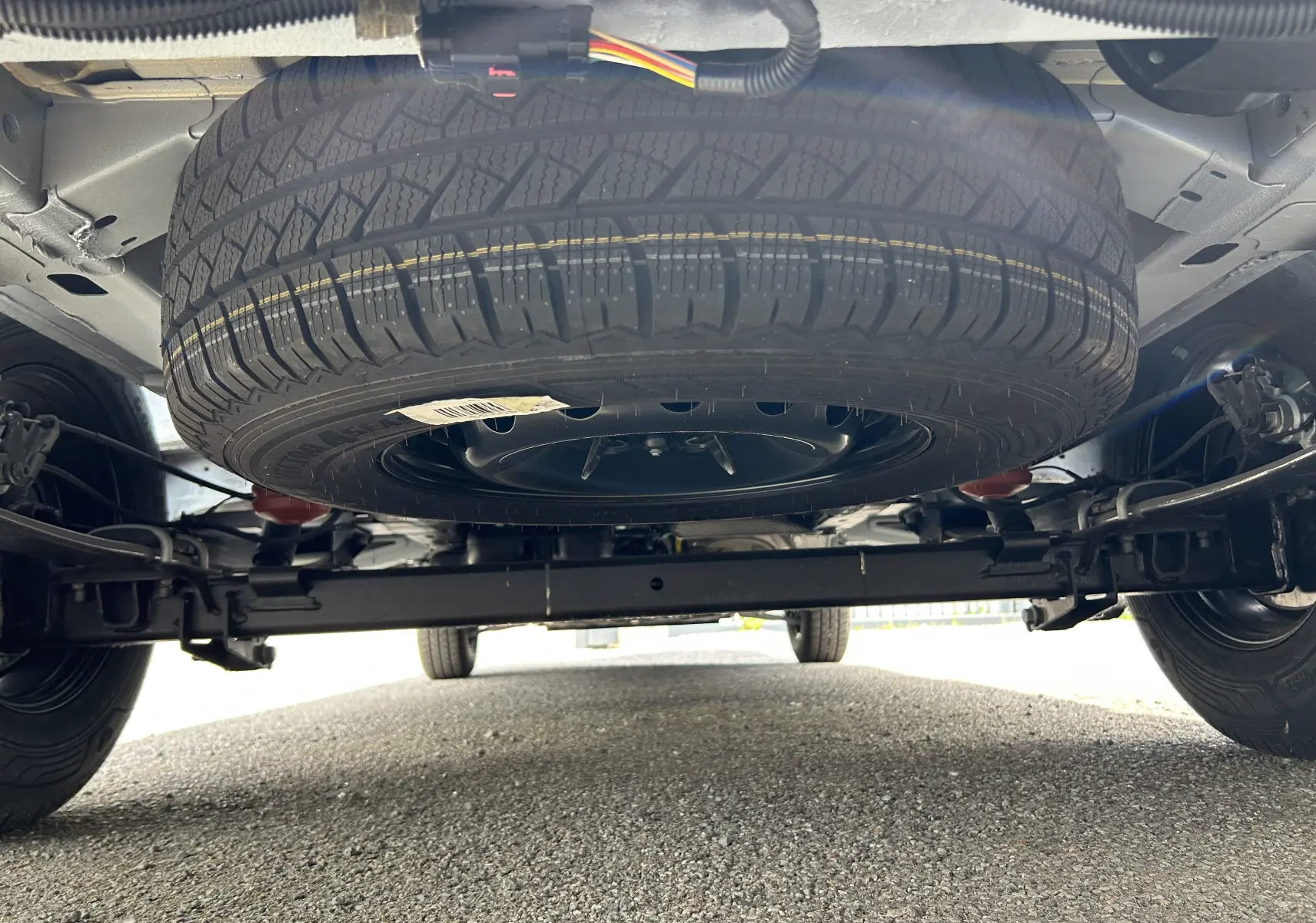 Vue en contre-plongée sous un Renault Master blanc montrant la roue de secours suspendue sous le châssis arrière.