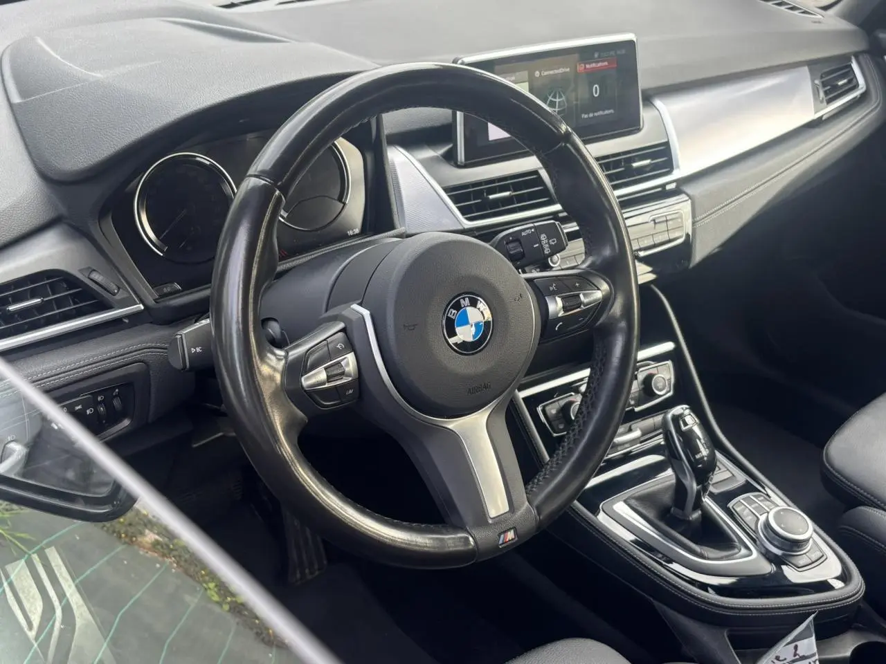 Vue intérieure centrée sur le volant cuir M et la console centrale d’une BMW Série 2 Active Tourer blanche.