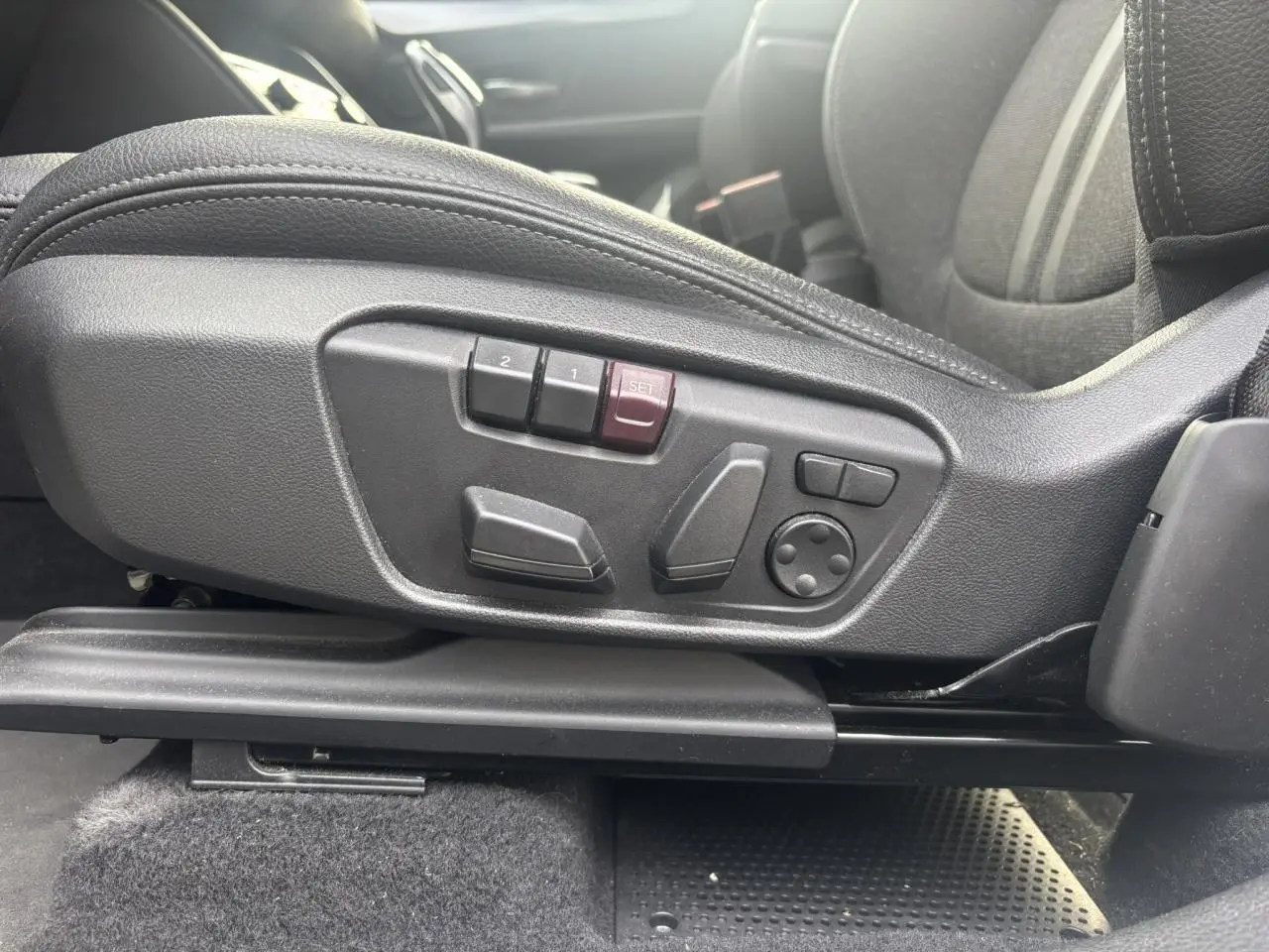 Gros plan sur les commandes électriques du siège conducteur noir dans une BMW Série 2 Active Tourer blanche.