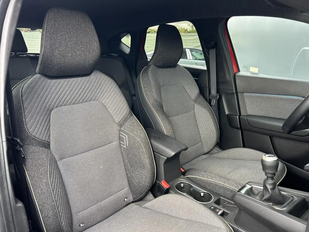 Vue intérieure côté conducteur du Renault Captur 2025, sièges gris avec coutures jaunes et levier de vitesse manuel.