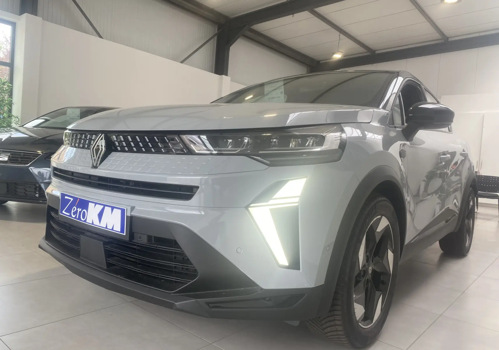 Renault Captur II 1.0 TCE 90CH TECHNO gris zinc métal vu en 3/4 avant droit avec feux LED allumés en showroom.