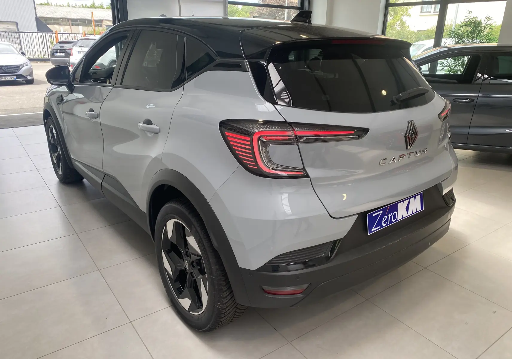 Vue 3/4 arrière droite du Renault Captur II gris zinc métal avec toit noir et feux arrière LED distinctifs en intérieur showroom.