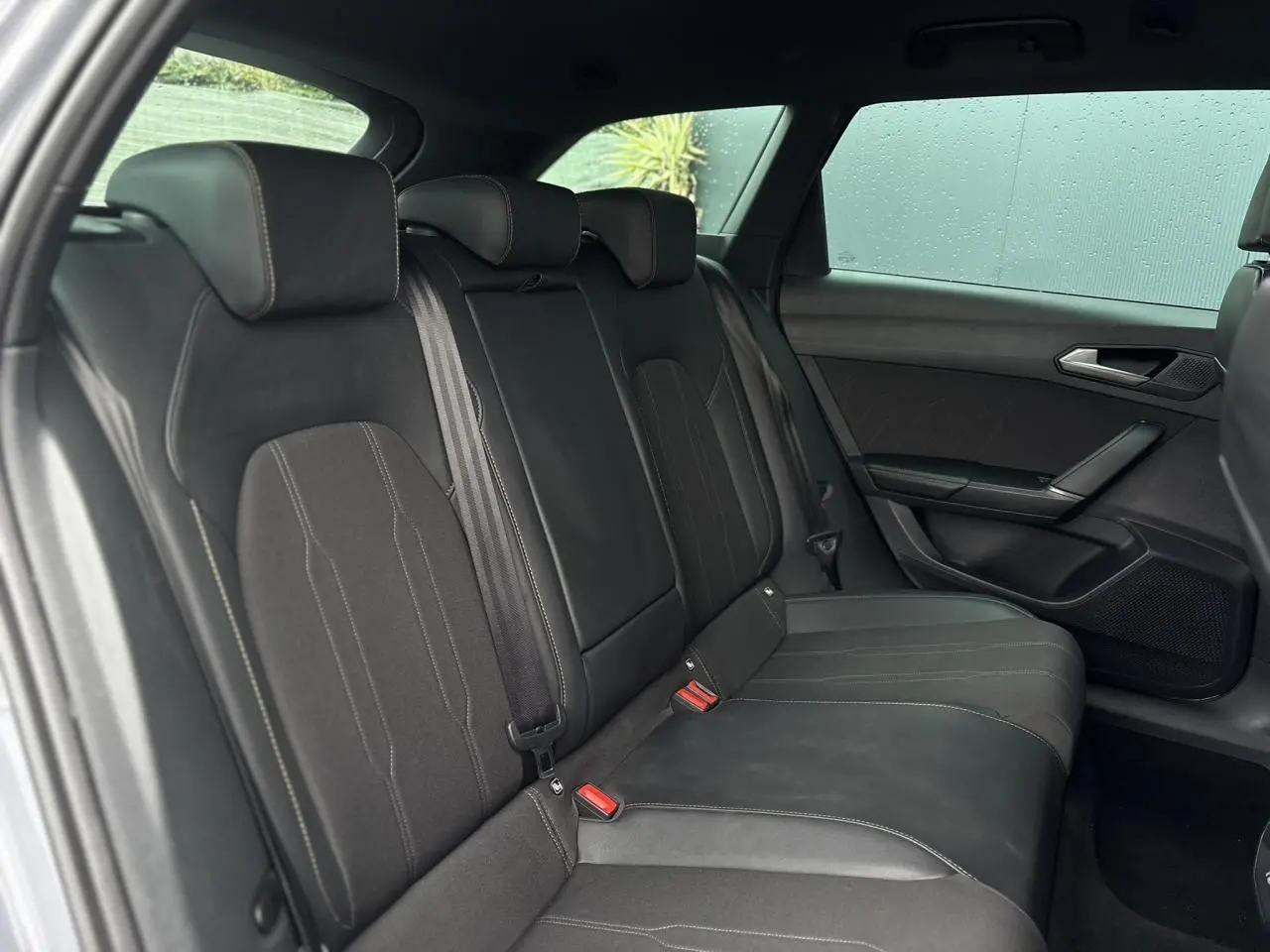 Vue côté droit des sièges arrière noirs en cuir et tissu du CUPRA LEON ST 2025 avec ceinture et appuie-têtes intégrés.