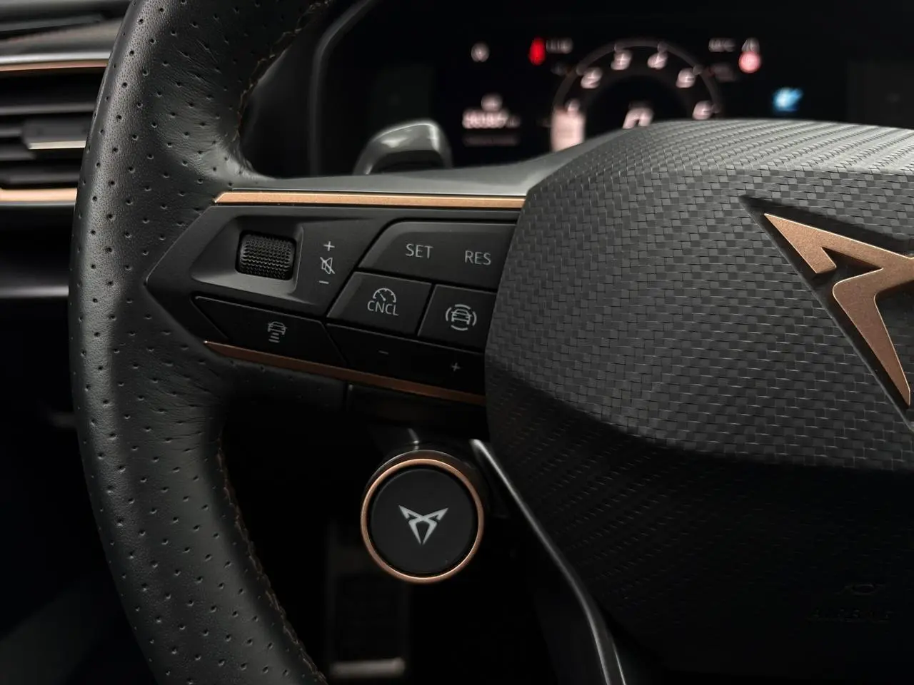 Gros plan sur le volant perforé noir avec logo CUPRA cuivré et commandes intégrées du Leon ST 2025.