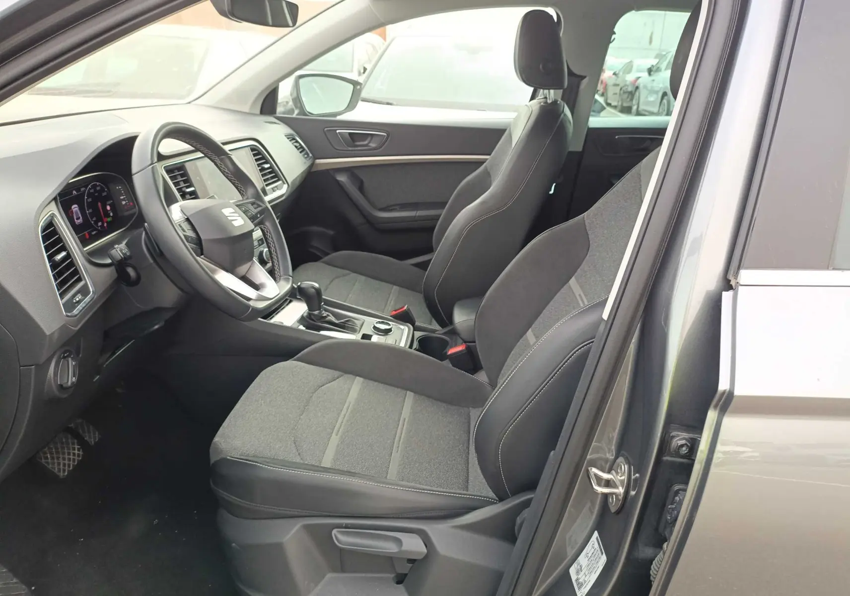 Vue intérieure côté conducteur du SEAT Ateca gris foncé 2023, montrant les sièges tissu et cuir, volant multifonction et console centrale.