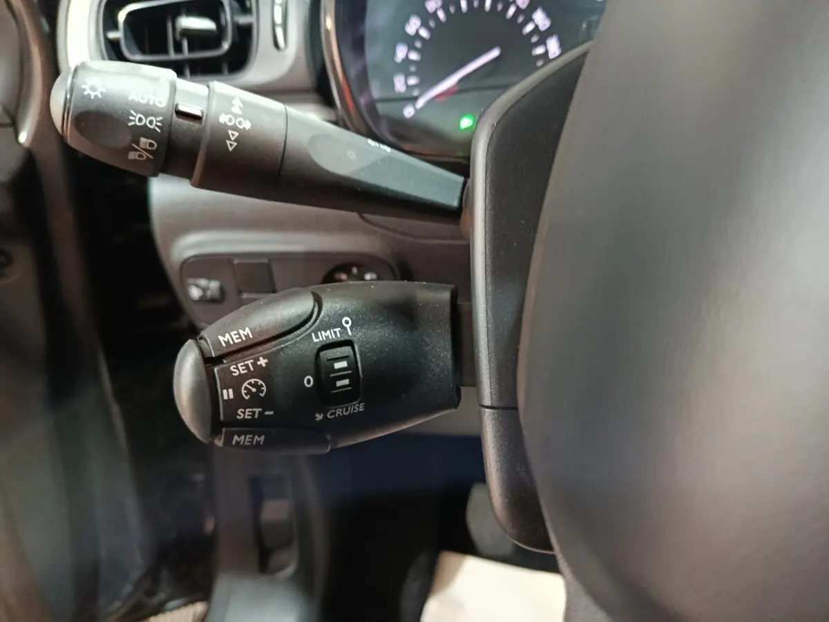 Gros plan sur la commande de régulateur de vitesse à gauche du volant dans l'habitacle d'une Citroën C3 gris foncé 2024.