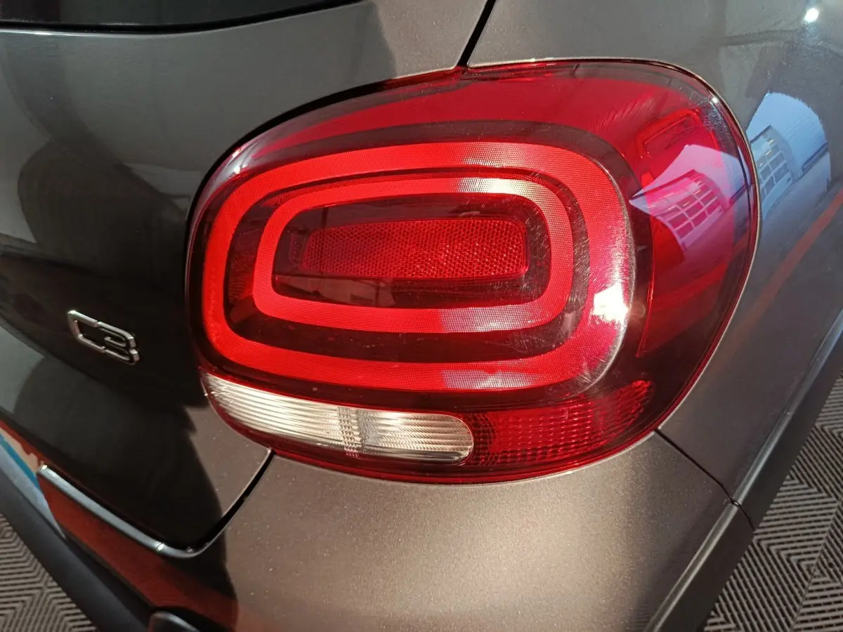 Gros plan sur le feu arrière droit rouge et blanc d'une Citroën C3 gris foncé, avec logo C3 visible sur la carrosserie.