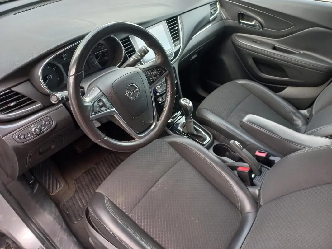 Vue intérieure côté conducteur de l’Opel Mokka X 2017, montrant le volant, la console centrale et les sièges en tissu gris foncé.