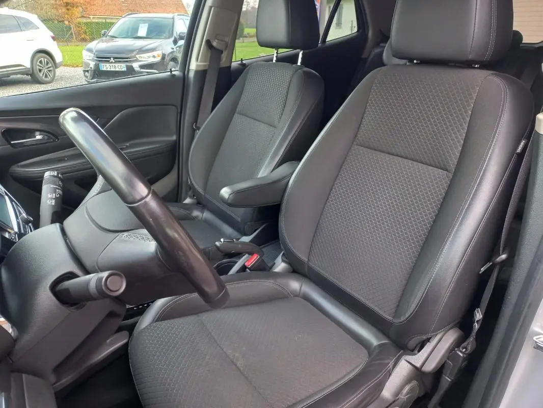 Vue intérieure côté conducteur de l’Opel Mokka X 2017, sièges noirs en tissu et cuir avec accoudoir central.