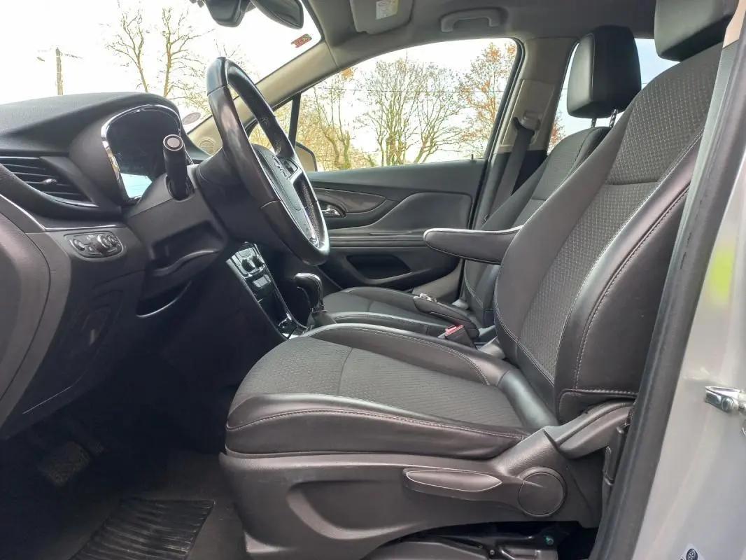 Vue intérieure côté conducteur de l’Opel Mokka X 2017, sièges tissu et cuir noirs avec accoudoir central.
