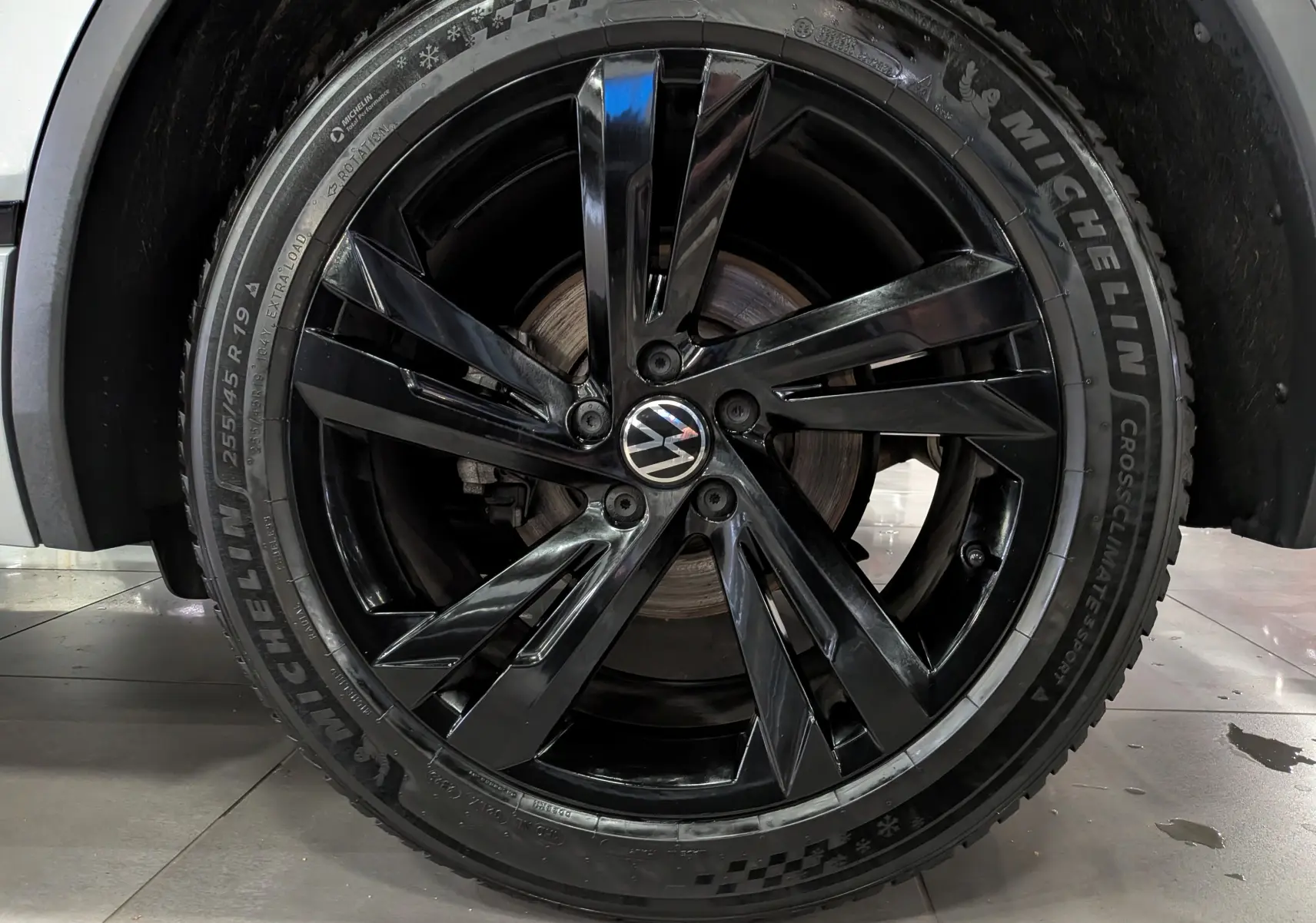 Gros plan sur la jante noire brillante de 19 pouces avec logo Volkswagen, montée sur un Volkswagen Tiguan reflet d'argent.