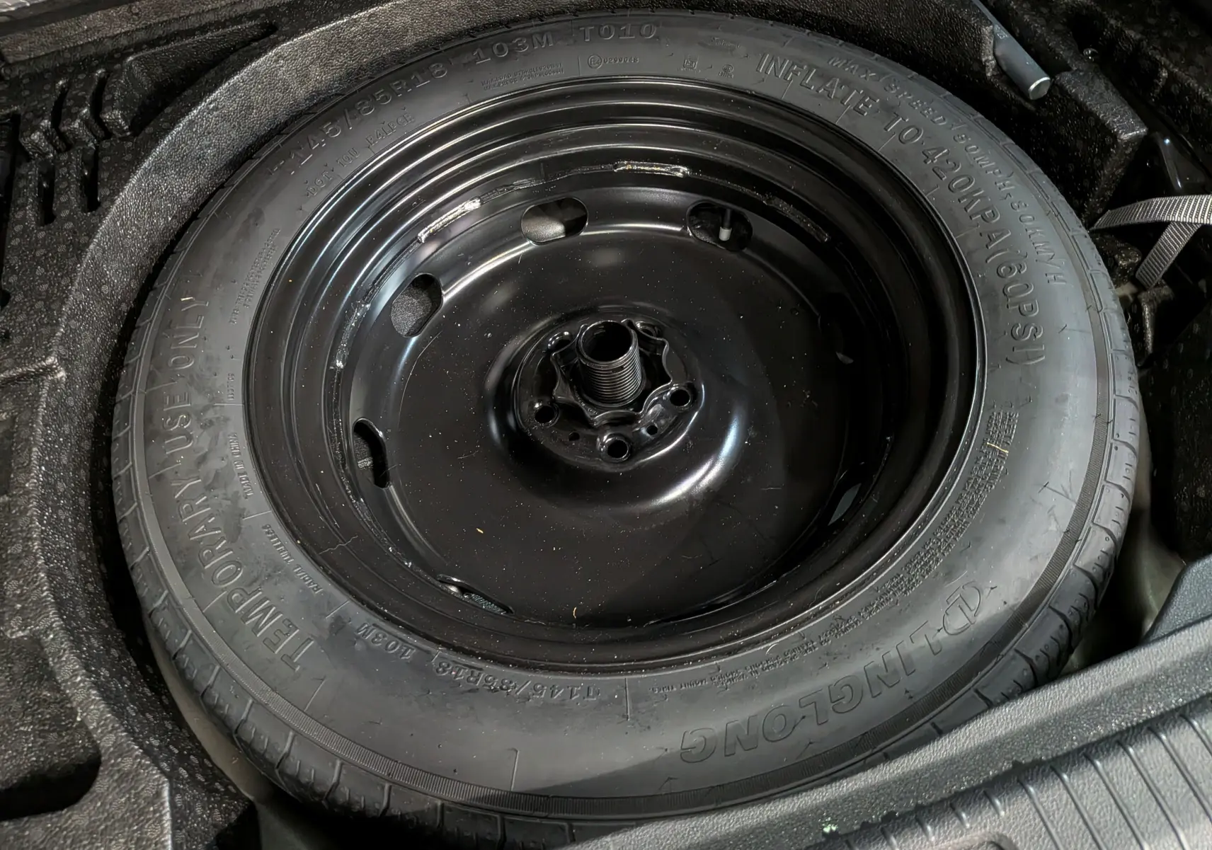 Gros plan sur la roue de secours noire logée dans le coffre du Volkswagen Tiguan 2024 reflet d'argent.