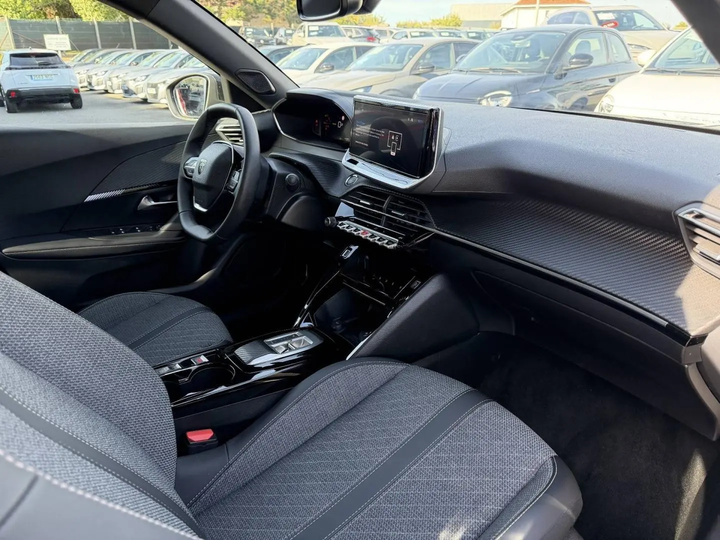Intérieur avant droit du Peugeot e-2008 2025, montrant sièges tissu gris et tableau de bord avec écran tactile central.