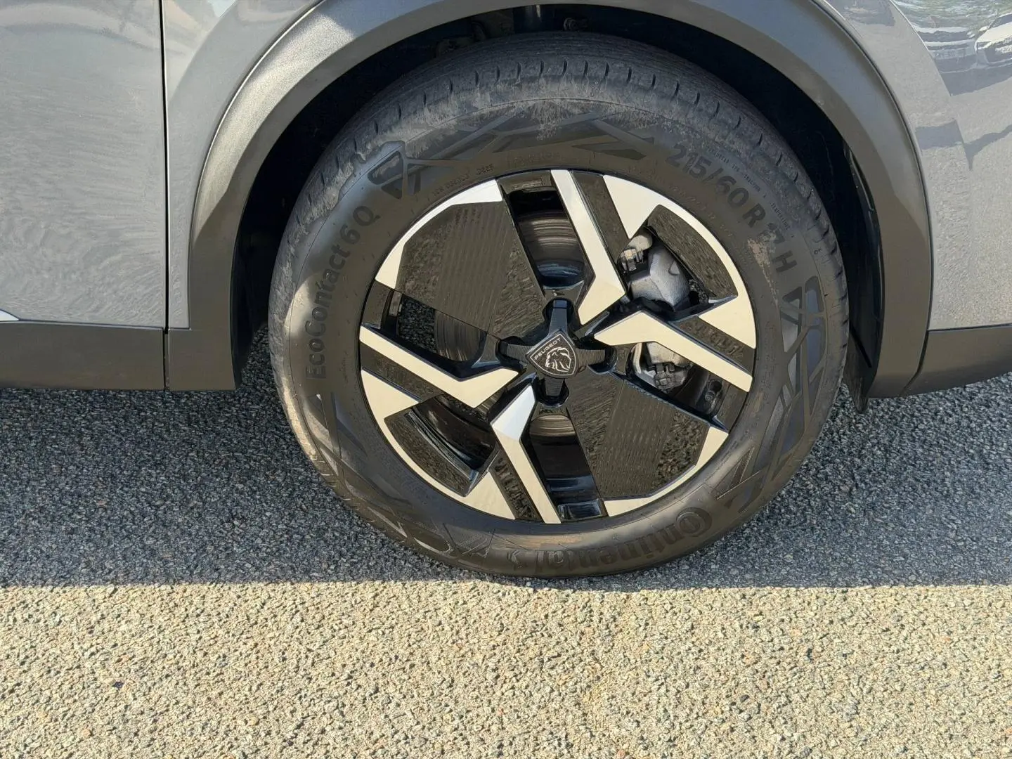 Gros plan sur la roue avant droite avec jante alu bicolore du Peugeot e-2008 gris Artense.
