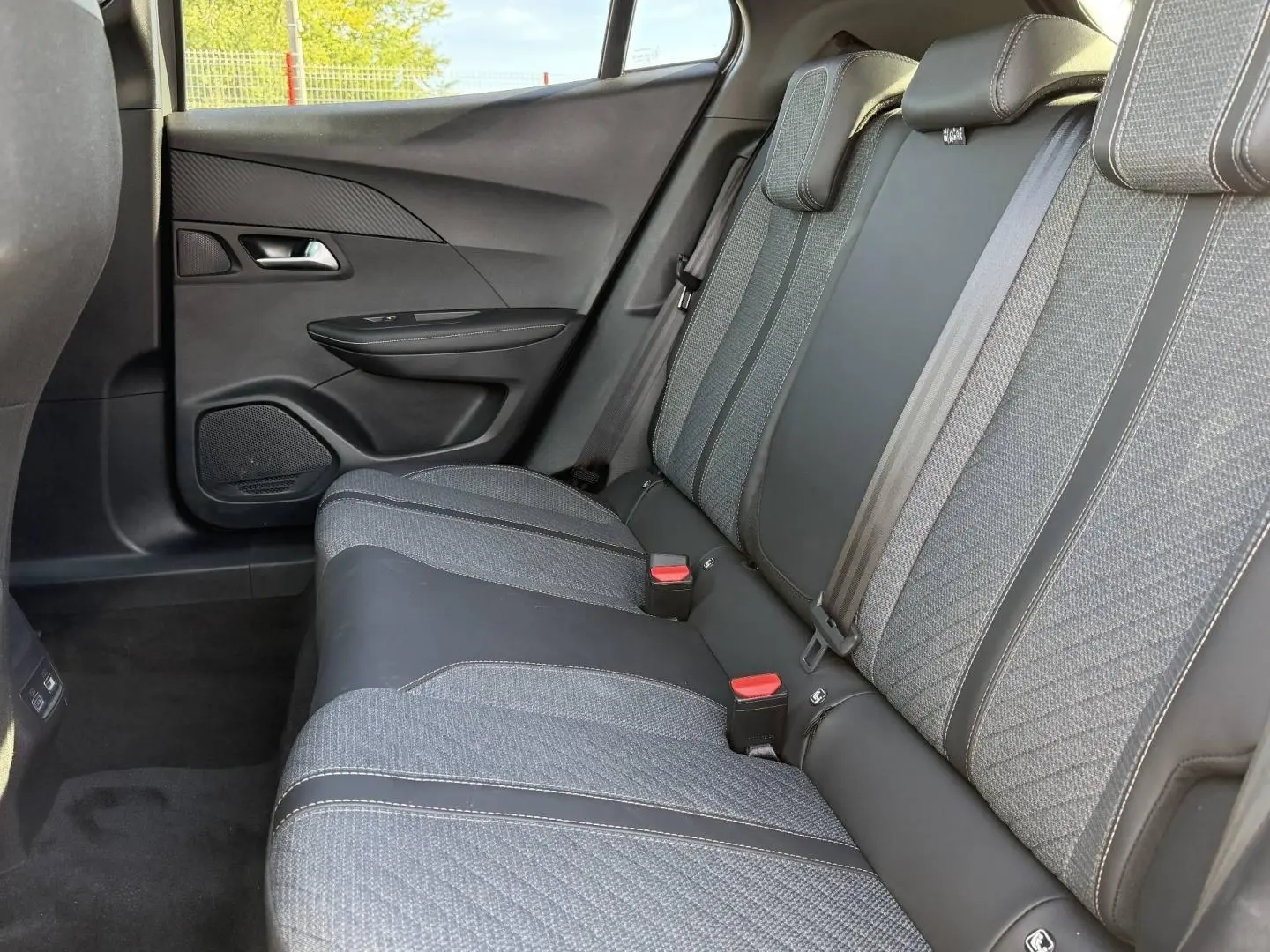 Vue latérale droite de la banquette arrière en tissu gris et cuir noir du Peugeot e-2008 2025, avec ceintures de sécurité visibles.