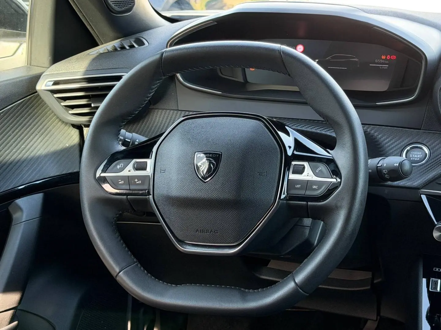 Vue rapprochée du volant multifonction noir de la Peugeot e-2008 2025 avec tableau de bord numérique en arrière-plan.