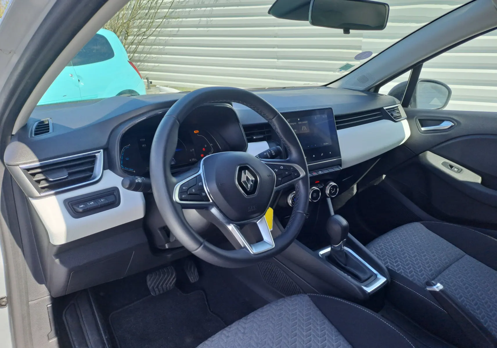 Intérieur avant droit de la Renault Clio V hybride 2022 avec tableau de bord gris clair et volant multifonction noir.