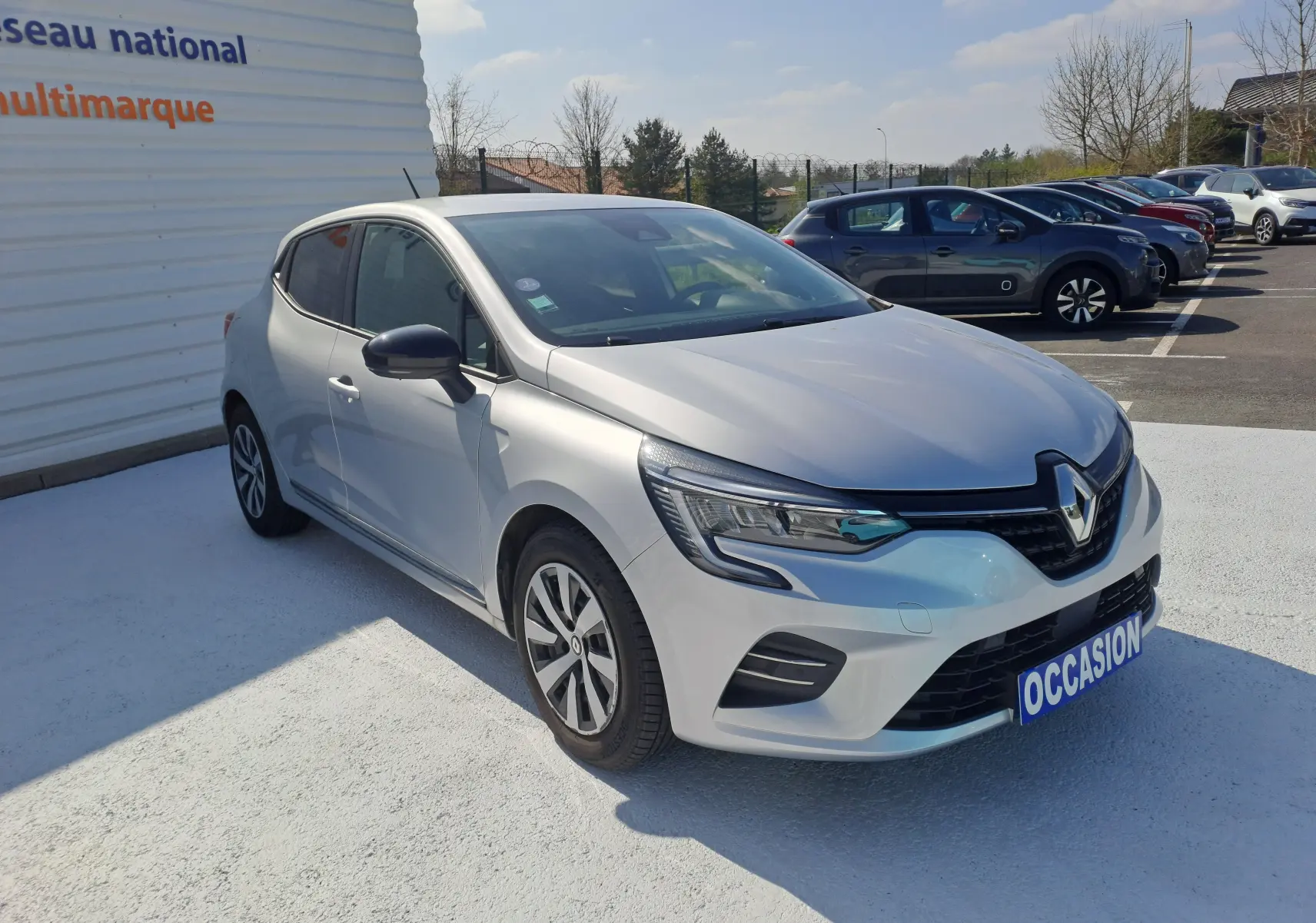 Renault Clio V gris Highland Metal vue 3/4 avant droit, avec phares LED et calandre noire brillante.