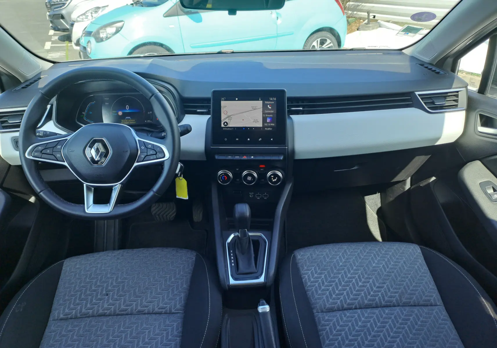 Vue intérieure avant de la Renault Clio V hybride 2022, tableau de bord gris clair avec écran tactile central et volant multifonction.