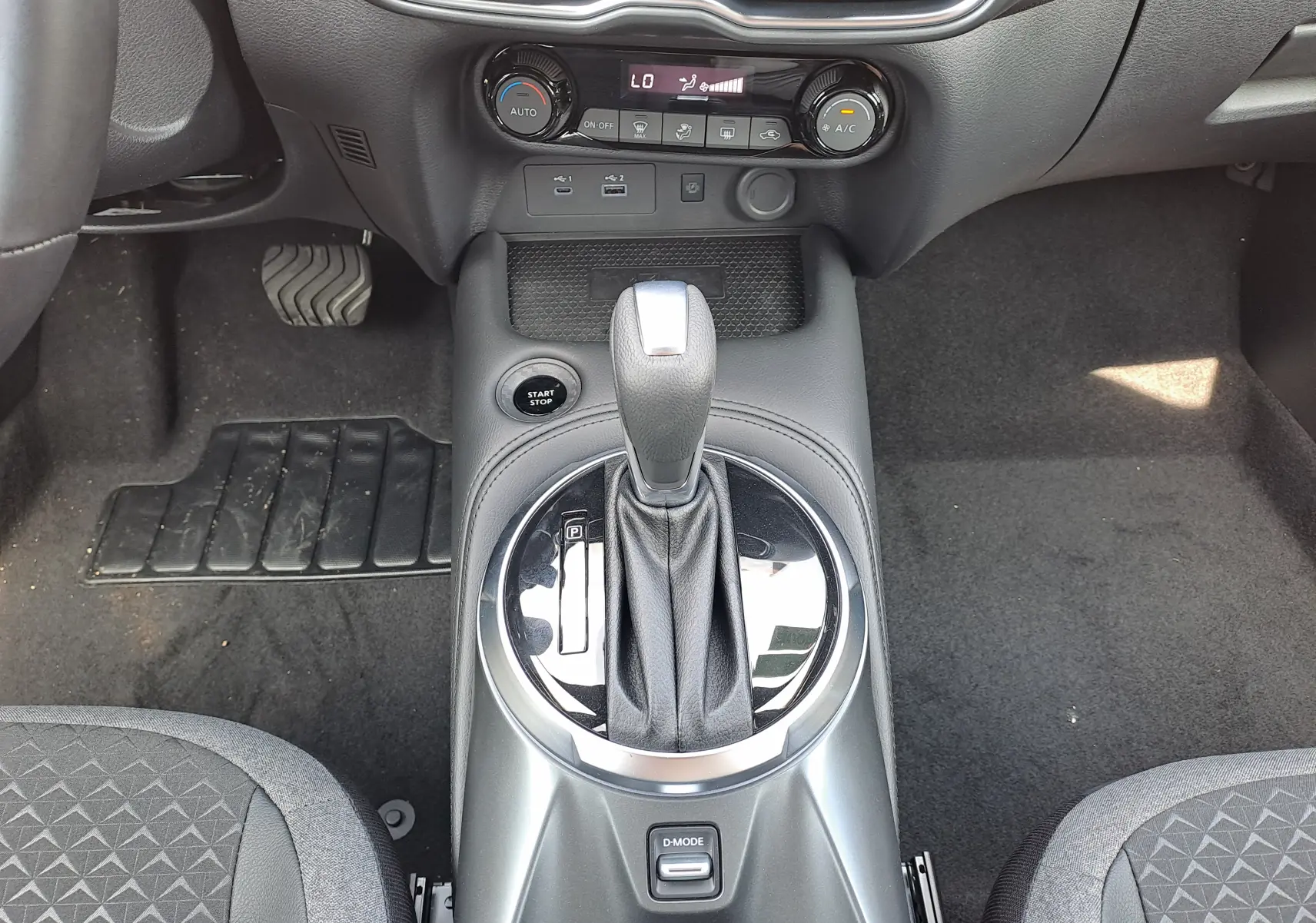 Vue rapprochée de la console centrale du Nissan Juke Hybrid 2025, avec levier de boîte auto et commandes climatisation.