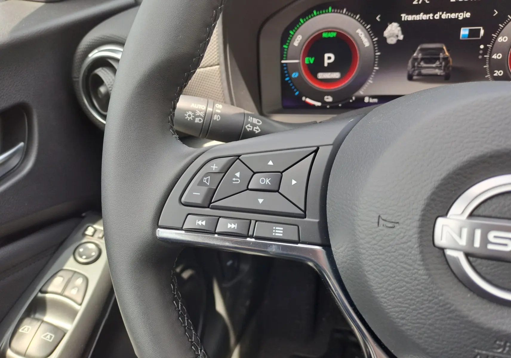 Gros plan sur le volant noir et les commandes intégrées du tableau de bord numérique d'un Nissan Juke Hybrid gris squale 2025.